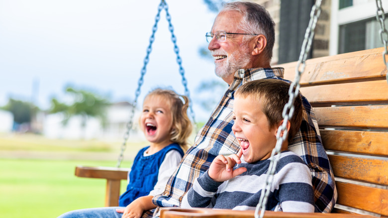 A senior man and two small children sitting on a porch laughing