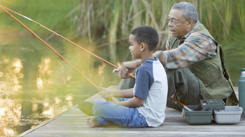 An elderly man and a young boy sitting on a dock fishing