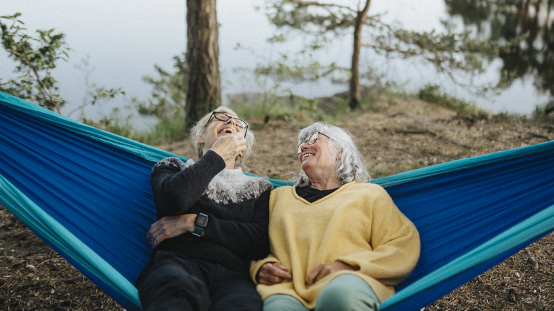 Two senior women laughing on a hammock in the woods