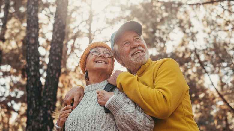 A smiling elderly man and woman hugging in a forest