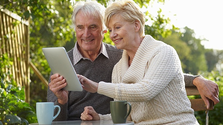 Couple smiling while sitting at garden table and reviewing tablet