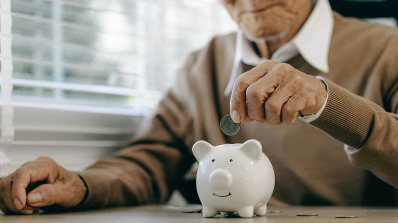 Old man putting money in a piggy bank