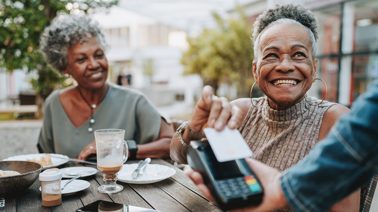 A smiling woman using her credit card to pay for an outdoor meal.