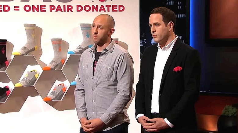 David Heath and Randy Goldberg on "Shark Tank" standing with hands folded next to Bombas display