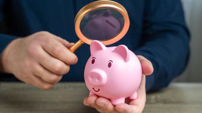 man holding magnifying glass over piggy bank