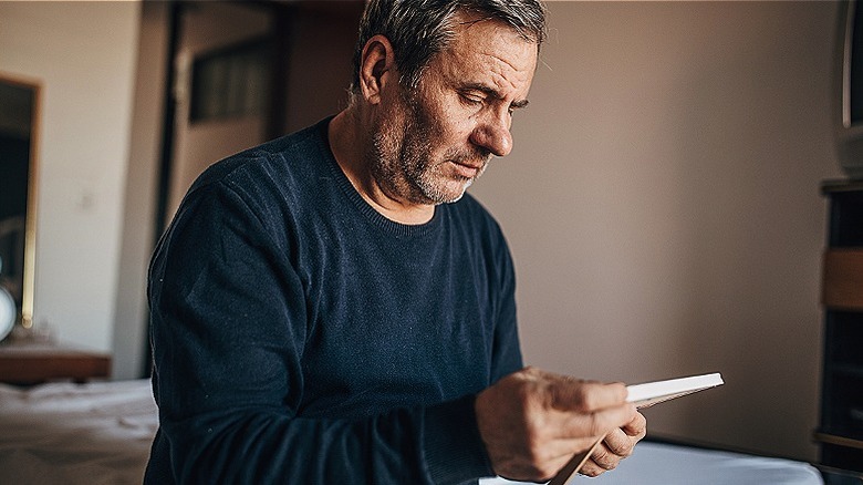 An older man sits in room staring at a photo in his hands