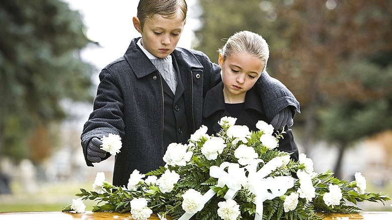 A young boy and girl laying flowers on a coffin at a funeral