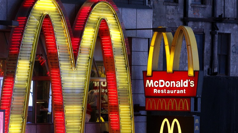 One large neon Golden Arches lit up in yellow with red trip and two smaller signs, one with the golden arches and the words 'McDonald's Restaurant' and another with just the golden arches lit up in yellow