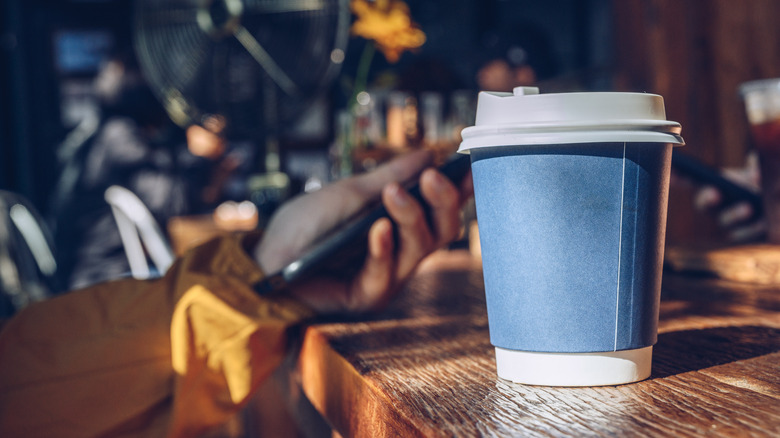 Person holding phone next to coffee cup