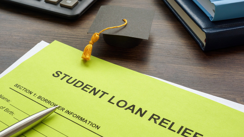 A small paper graduation caps rests on a desk near a lime-green student loan relief form.