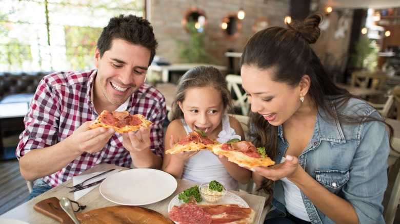 A man, woman and child smiling while eating pizza at a restaurant