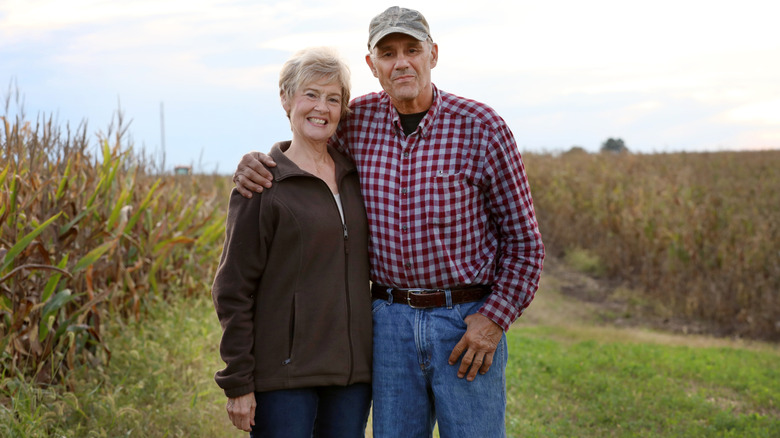 An smiling elderly couple standing in a farmer's field