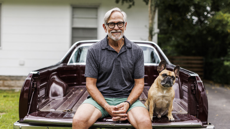 A smiling senior man sitting in the back of a pick up truck with his dog