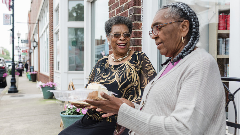 Two smiling elderly women sitting on a bench eating cake