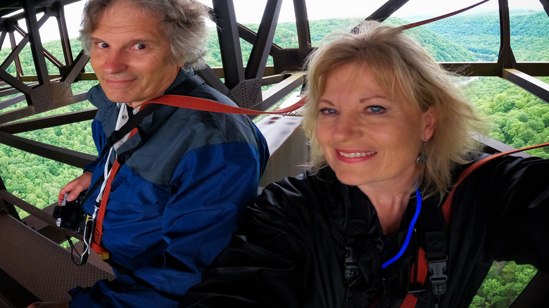 A Boomer couple taking a selfie on a bridge over a forest