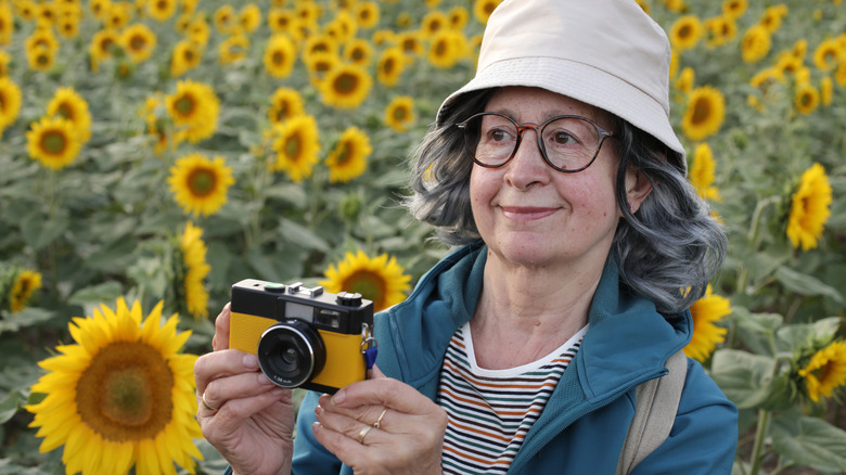 A senior woman standing in a field of sunflowers with a camera