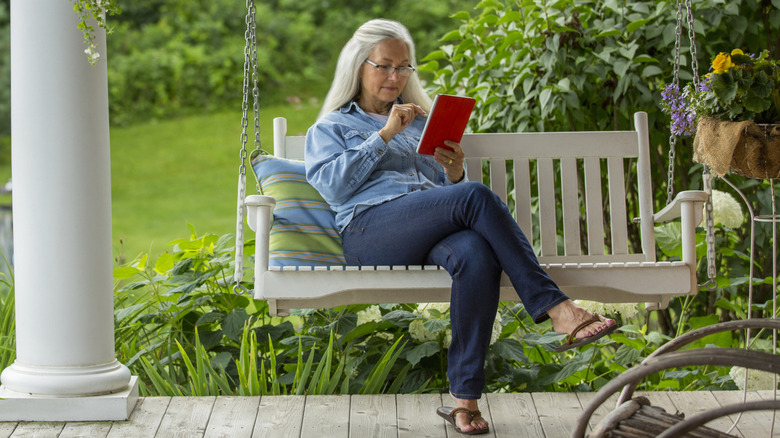 A Boomer woman sitting on her front porch reading her Kindle