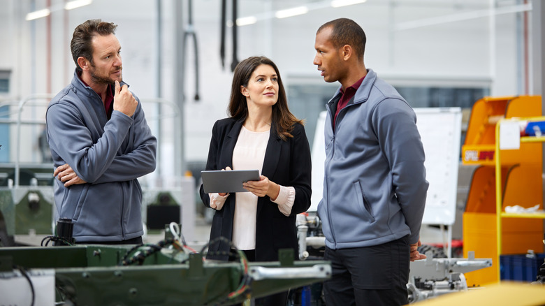 Three auto professionals standing at a car production line