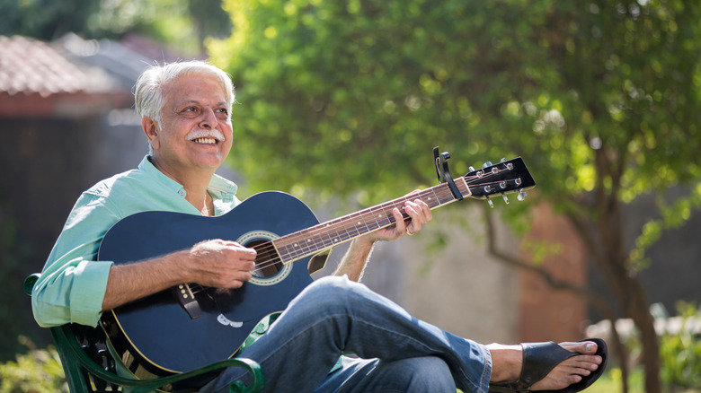 Portrait of senior man playing guitar sitting at garden.