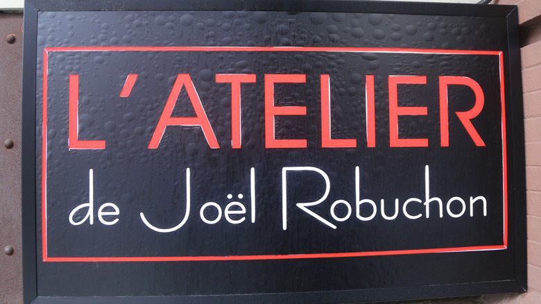 Sign for L'Atelier de Joel Robuchon, red and white words on black background.