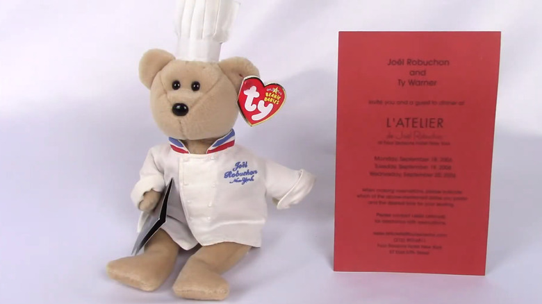 Chef Robuchon Beanie Baby and red L'Atelier invitation against a white background.