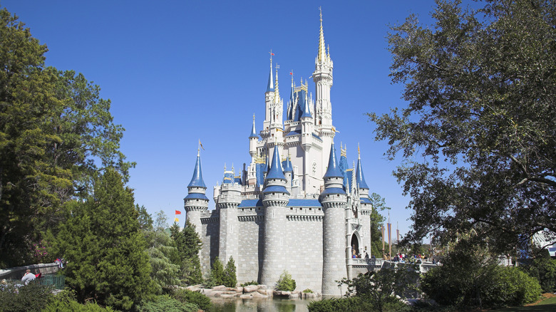 A side profile of Walt Disney World's famous Cinderella Castle, flanked by trees and tourists.