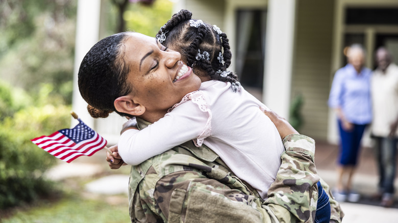 Uniformed woman holding child in front of home.