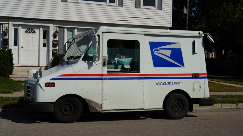 A U.S. postal service mail truck parked in front of a suburban home