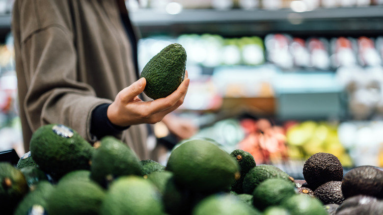 Person shopping for avocados at grocery store