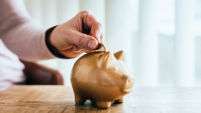 Person putting a coin into a golden piggy bank