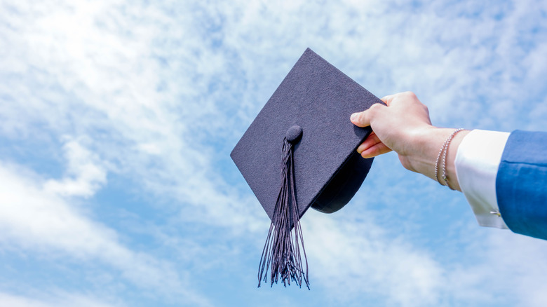 Close up shot of graduate holding his cap into the sky