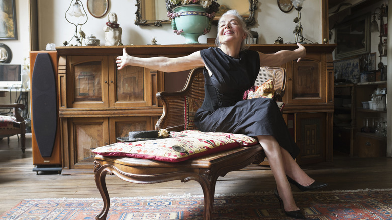 An senior sitting on an antique chair with arms spread apart