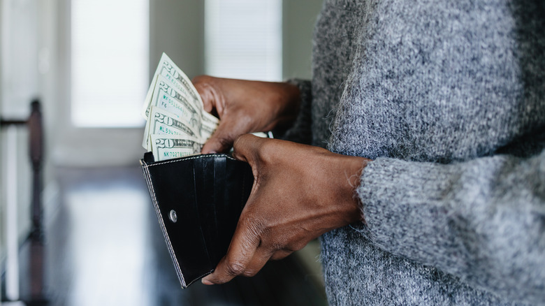 A woman removing several twenty-dollar bills from a wallet.