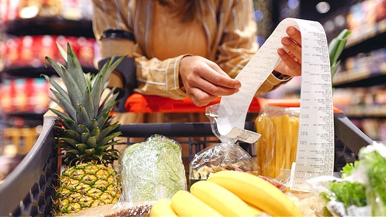 Person reviewing receipt while leaning on full shopping cart