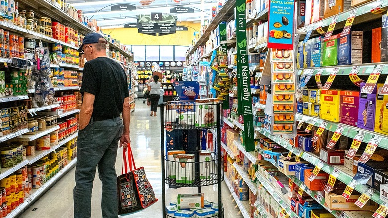 Shopper holds reusable bag in grocery aisle while looking at cans