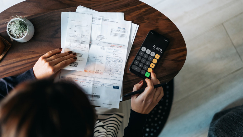 Person looking at documents and using calculator at table.