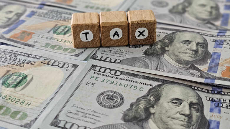 Wood blocks spelling the letters tax on top of several US hundred dollar bills