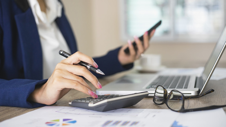 Professional woman making calculations on desk with calculator.