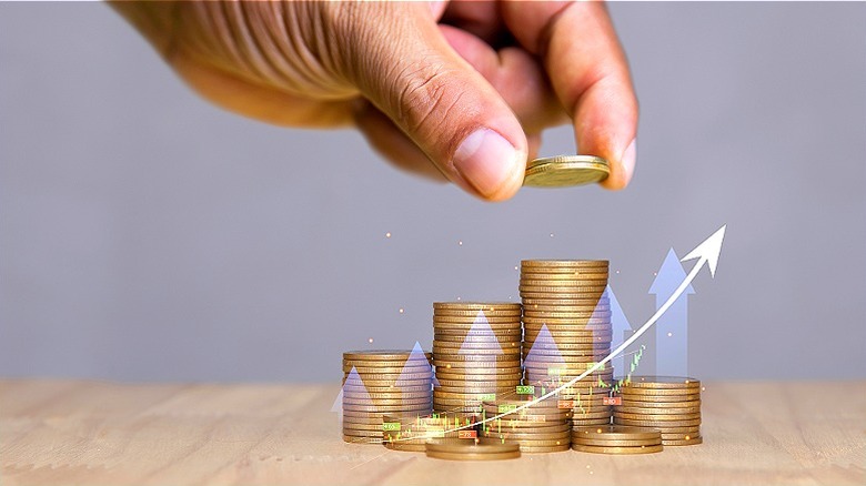 Hand placing two coins on coin stack with an upward arrow