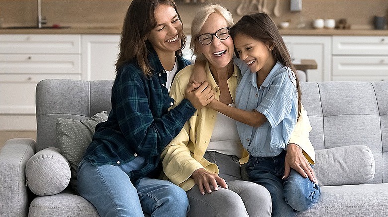 Three generations seen laughing, sitting on couch in family room