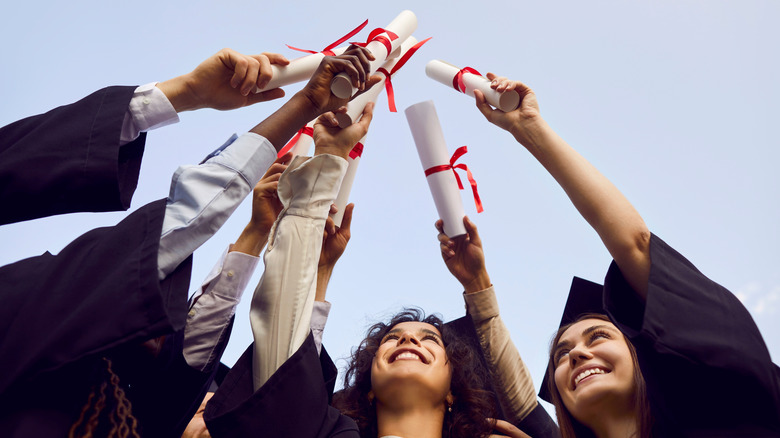 Happy college graduates holding their diplomas in the air together