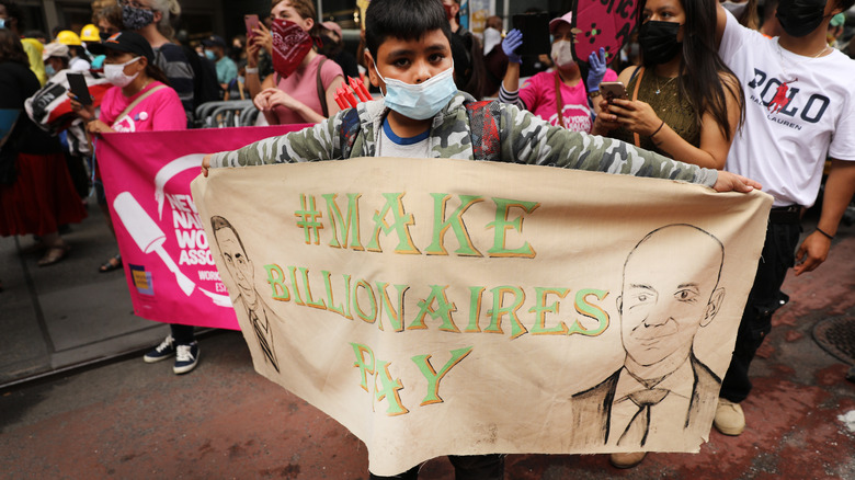 Young protester holds up banner calling for a tax on the rich