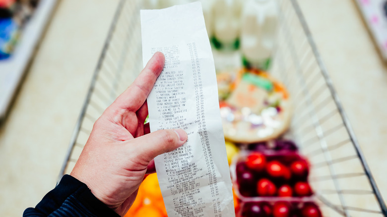 Person reading grocery store receipt over cart