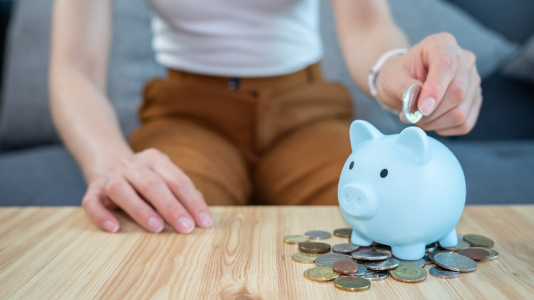 A person depositing a coin into a blue piggy bank.