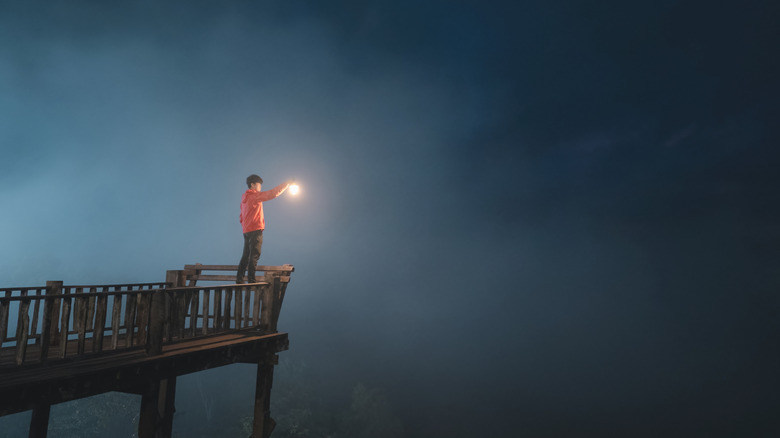 man on platform looking into fog and holding a lantern