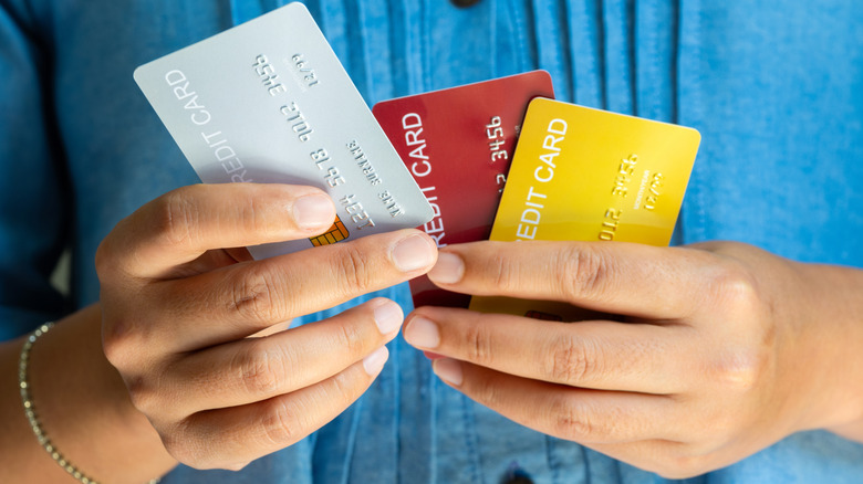 The torso and hands of a person holding three different nondescript credit cards.