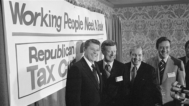 President Ronald Reagan and group smiling in front of tax cut sign