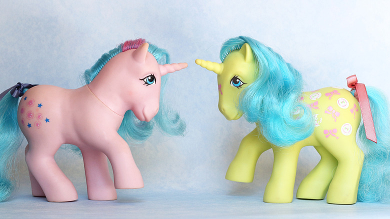 Vintage unicorn My Little Pony toys face off in a friendly staring contest, against a white background.