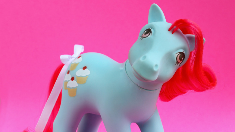 A vintage G1 Cherry Sweet pony, with red mane and cupcake cutie mark, gazes into the camera's eye, against a hot pink background.