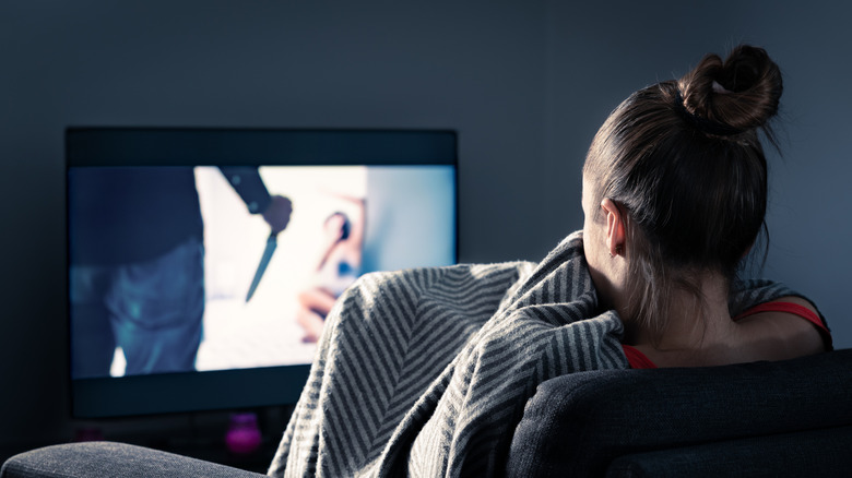 Woman watching scary movie with television screen showing person holding knife